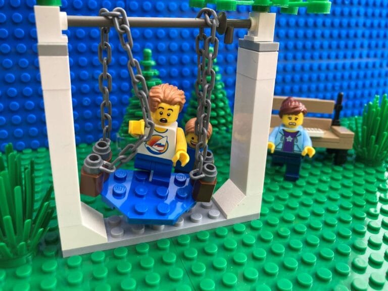 Child taking risks by doing a trick on a swing by not holding hands. Mum looking worried in the background