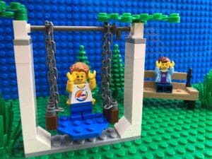 Child playing on a swing but not holding onto any of the ropes. Mum looking worried behind at the risk taking behaviour