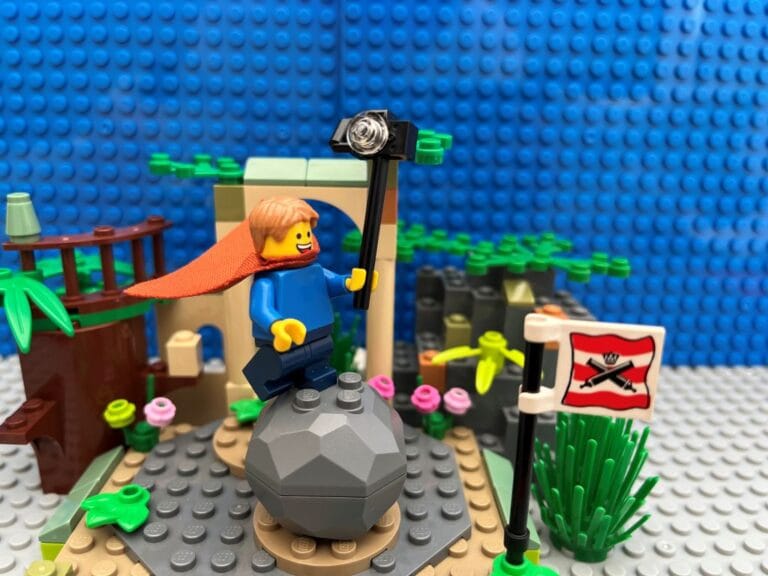 A child standing on a rock, with a cape and a selfie stick with a camera on the top making a stand