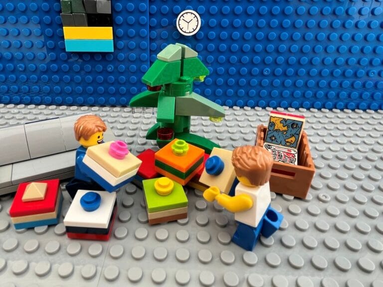 Two children placing a selection of brightly coloured Christmas presents under a Christmas tree.