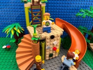 Child standing at the top of the climbing frame looking worried while two parents stand at the bottom trying to build confidence