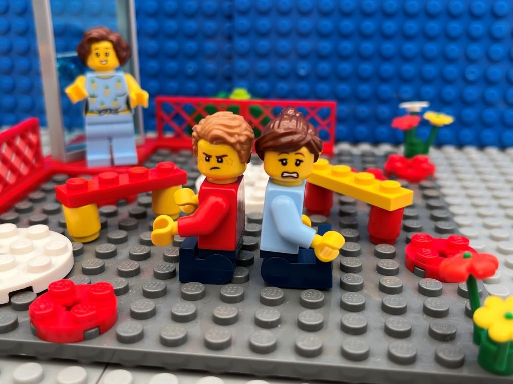 Mum and small child sitting back to back in front of the school gates, both struggling with school drop separation anxiety